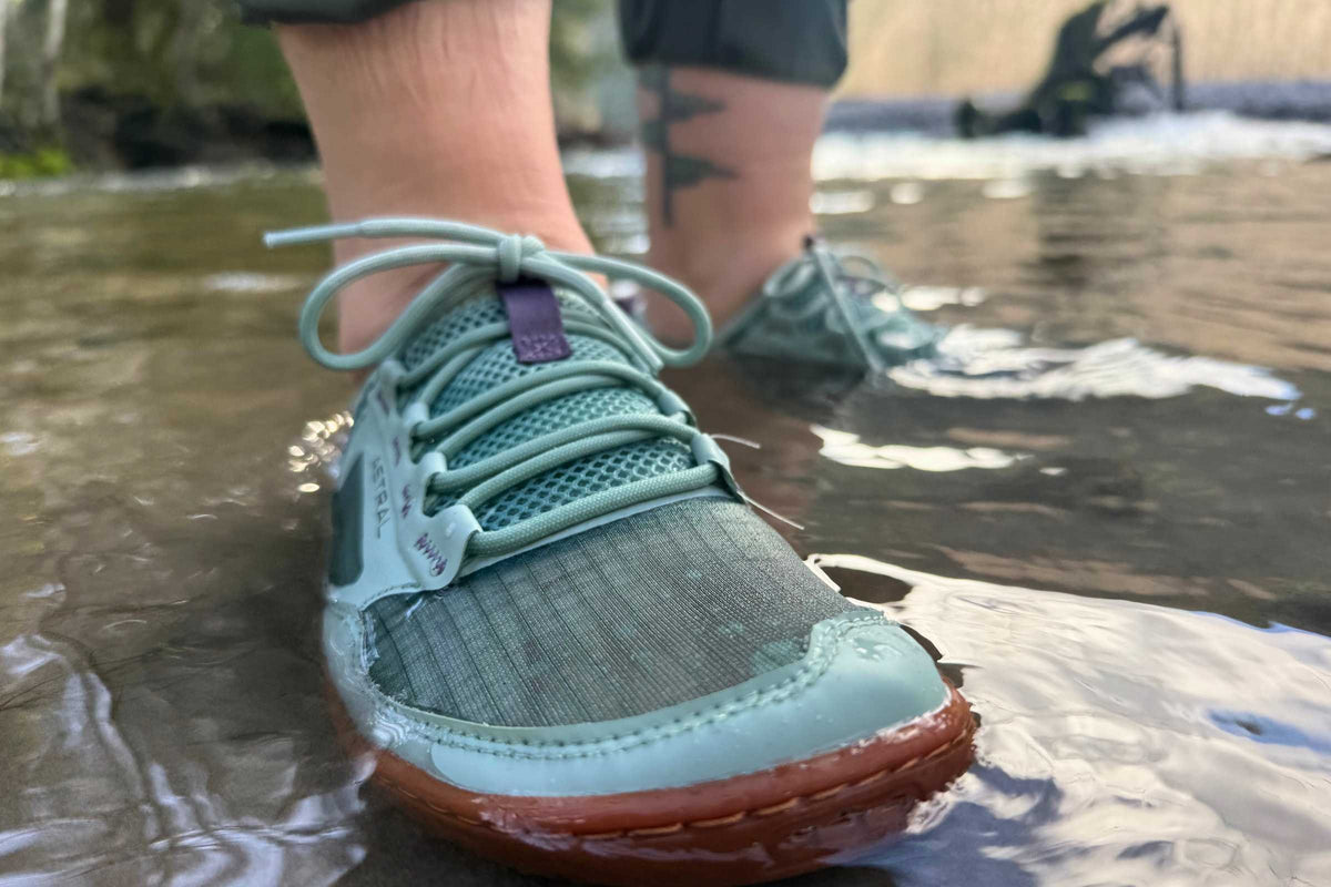 Astral Loyak AW shoes in mint green, worn by a person standing in shallow water, showcasing their water-friendly design.