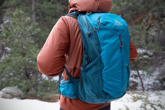 Gregory Zulu 24 LT blue hiking backpack worn by a person in a winter landscape with trees.