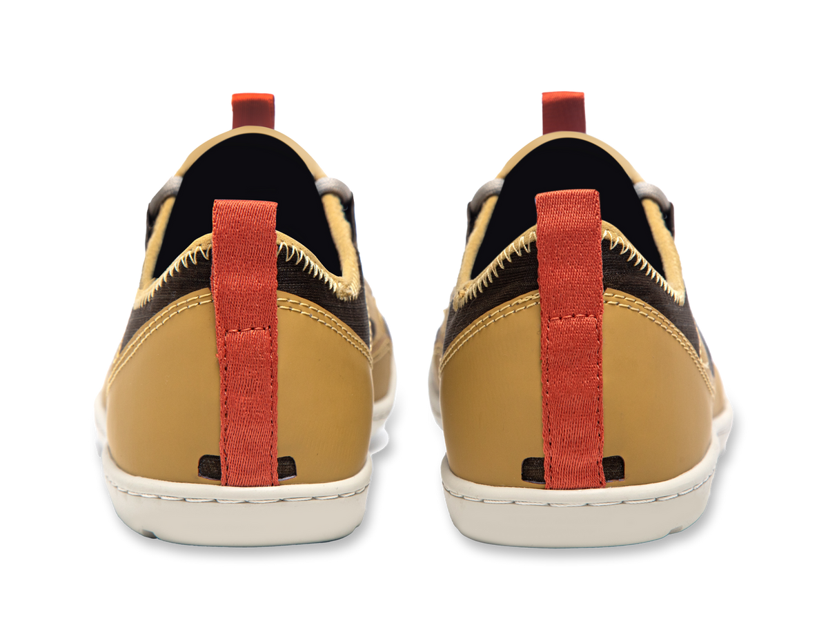 Back view of two Loyak AC | Astral shoes, tan with red pull tabs and white soles, on a black background.