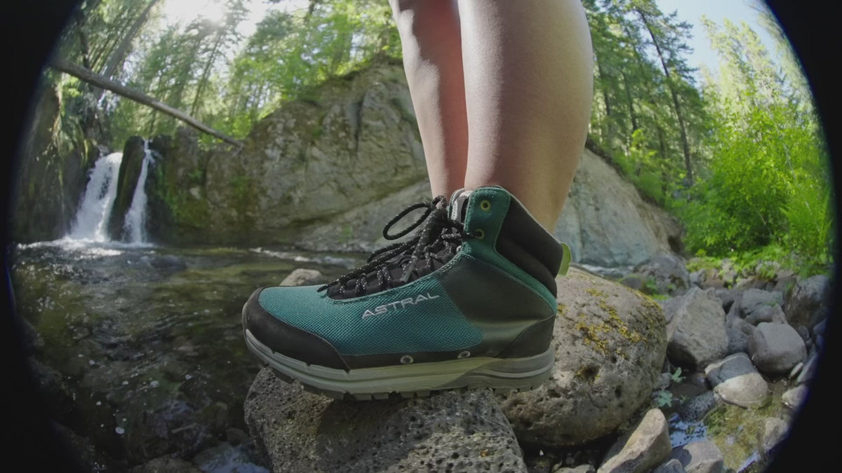 Astral Tr1 Merge shoe in teal on a rock, with a waterfall and lush green forest in the background.