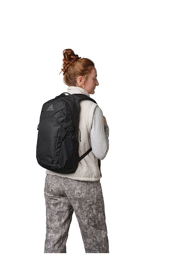 Black Gregory Signal 20 backpack worn by a person, seen from the back. The person is wearing a light vest and patterned pants.